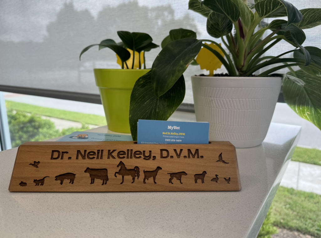 Wooden nameplate with "Dr. Neil Kelley, D.V.M." carved alongside animal silhouettes, flanked by potted plants.