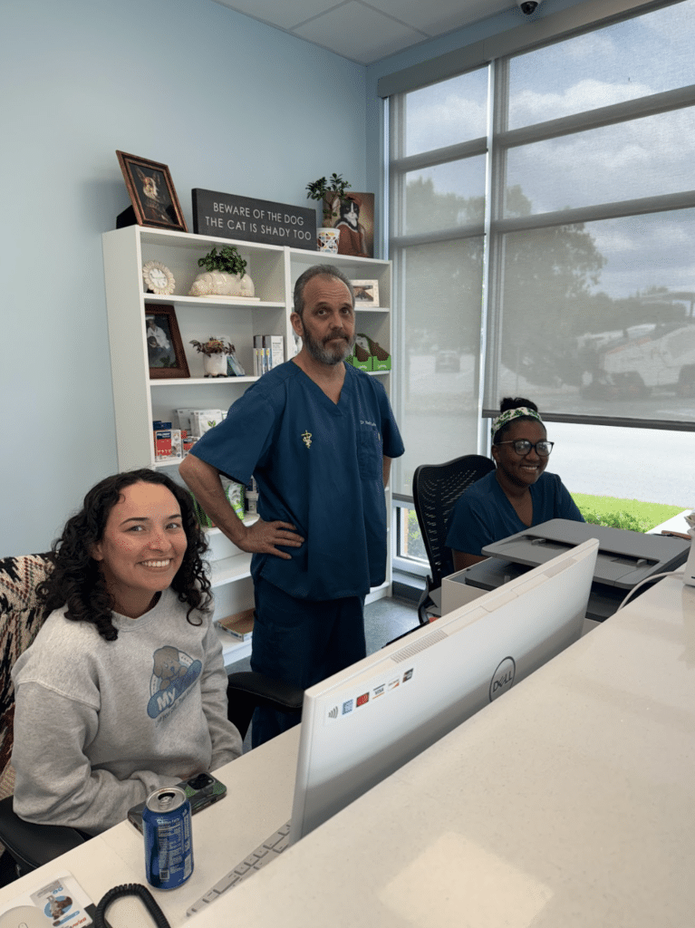 Three people smiling in a vet clinic reception area.