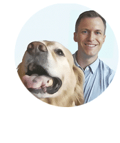 A man smiling behind a golden retriever sticking its tongue out.