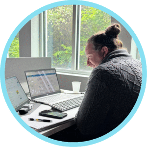 Man working on a laptop at a desk near a window smiling.